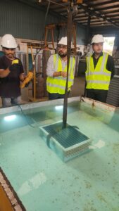 Three workers in safety gear inspecting a heat exchanger submerged in a water tank at an industrial facility.